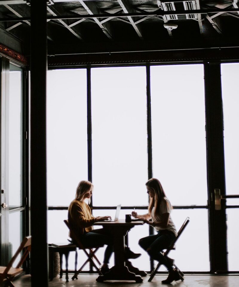 Two people in conversation across a table by a window